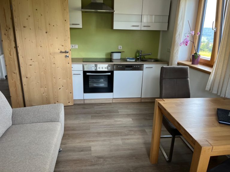 Wohnküche mit 2-Sitzer-Sofa und Esstisch Helle Wohnküche der Ferienwohnung Neyer in Steibis mit Esstisch, Sofa und Blick ins Grüne – natürlich wohnen im Allgäu